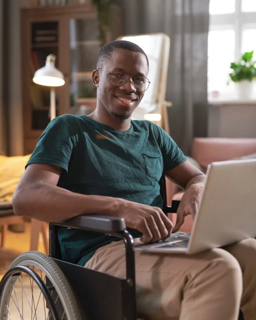 Disabled man in wheelchair with laptop smiling at camera